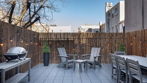 Een terras buiten met een betegelde vloer, houten meubels en een bamboescherm.