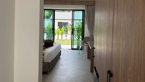 Ein Schlafzimmer mit Bett, Sessel und Blick auf einen Garten durch große Glasfenster.