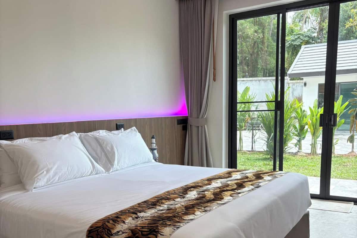 A modern bedroom with a large bed, a view of the outdoors, and a purple-lit ceiling.