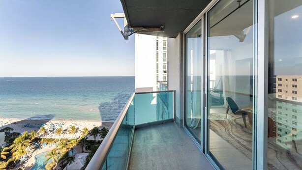 Un balcon doté d’une rambarde en verre, offrant une vue sur une plage et l’océan.