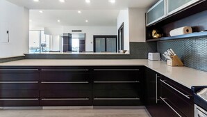Une cuisine moderne avec des meubles de couleur sombre, un pare-feu en carreaux et un plan de travail sur lequel on trouve un grille-pain et un bloc à couteaux.