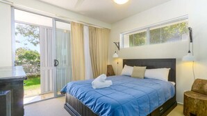 Een slaapkamer met een groot bed, een schuifdeur naar buiten, een klein houten krukje en een plafondventilator.