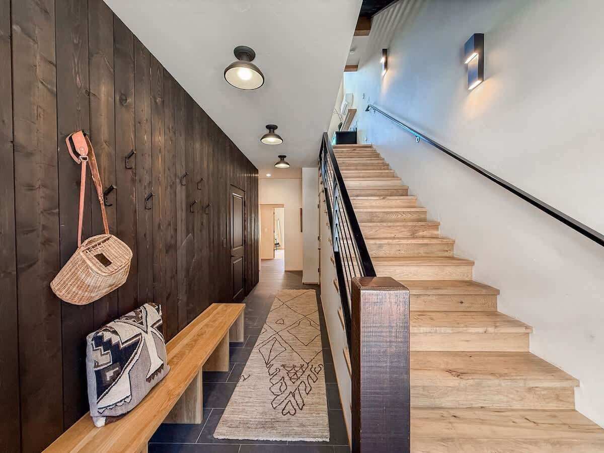 A wooden staircase with a handrail, a bench, and a patterned rug leading to a room.