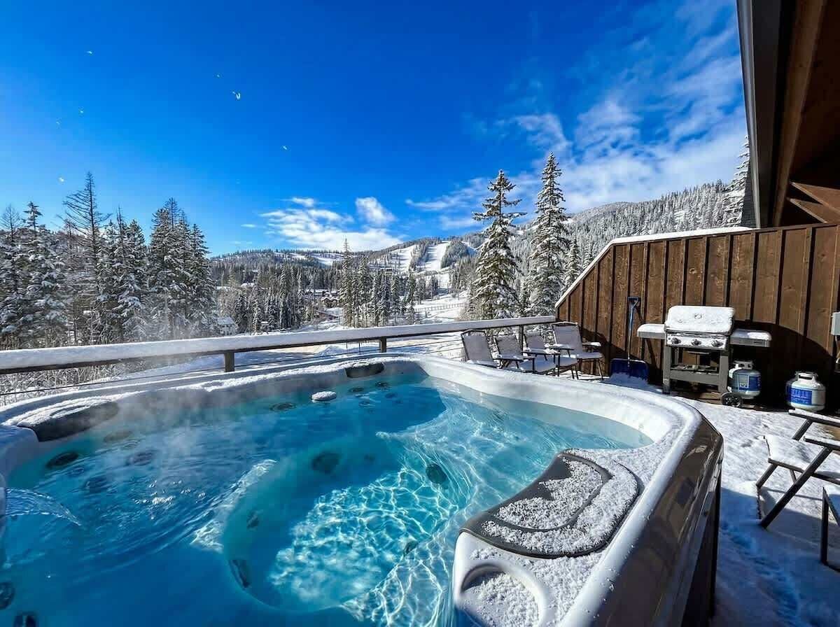 A hot tub with a clear view of snowy mountains and a wooden deck with chairs.