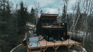 A modern cabin with a wooden deck, a hot tub, and a fireplace. - Ökohaus Mont-Tremblant: Private Luxury Nordic Eco Cabin with Spa & Sauna (La Conception)