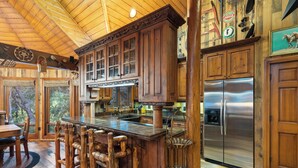 A rustic kitchen with wooden cabinets, a stainless steel refrigerator, and a bar area with stools. - SUNNYSIDE, FLAT YARD, HOT TUB, MOUNTAIN VIEWS, WOOD BURNING FIREPLACE (Sundance)
