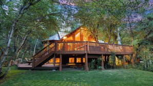 A wooden cabin with a deck and stairs, surrounded by trees. - SUNNYSIDE, FLAT YARD, HOT TUB, MOUNTAIN VIEWS, WOOD BURNING FIREPLACE (Sundance)