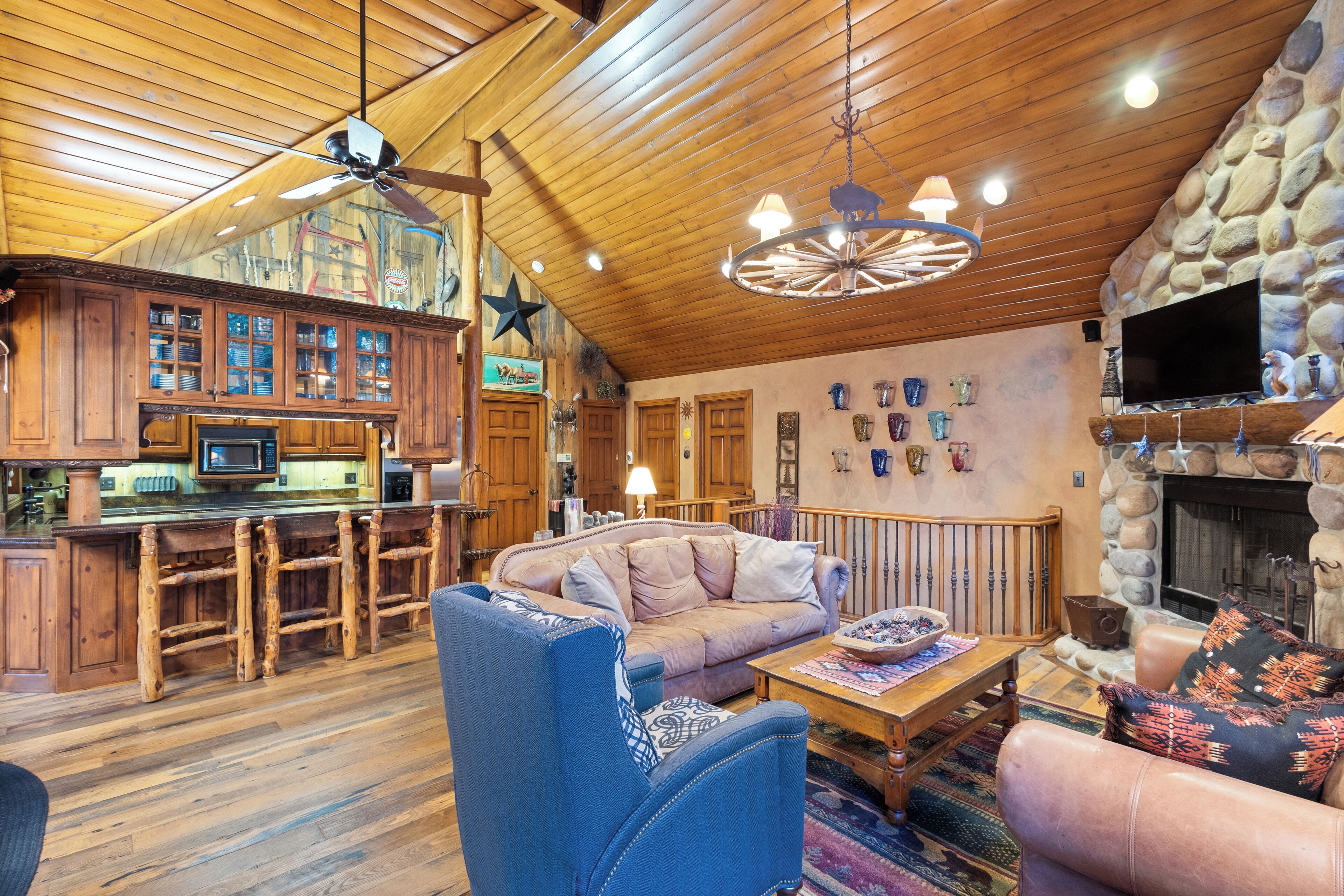 Un vaste espace de vie agrémenté d’une cheminée en pierre, d’un plafond en bois et d’un coin bar avec des tabourets en bois.