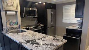 Een moderne keuken met donkere kasten, een groot granieten eiland, roestvrijstalen apparatuur en inbouwspots.