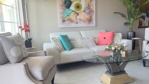 Een woonkamer met een witte bank, een glazen salontafel en een plafondventilator.