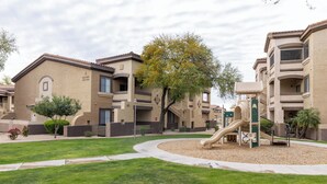 A residential building with a playground, including a slide, surrounded by well-maintained lawns and trees. - Cozy 2-Bedroom Condo with Mountain View, Hot tub and Heated Pools (Mesa)