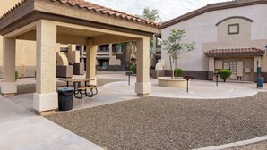 A courtyard with a covered seating area, a trash bin, and a small tree. - Cozy 2-Bedroom Condo with Mountain View, Hot tub and Heated Pools (Mesa)