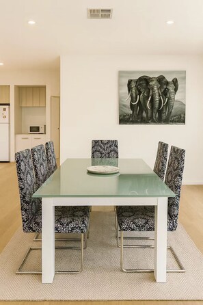 Een eetgedeelte met een glazen tafel, gestreepte stoelen, een bord en een olifant schilderij aan de muur.