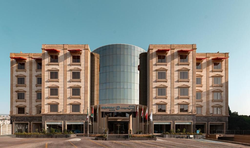 A hotel with a central glass tower and symmetrical wings, featuring a formal entrance with flags.