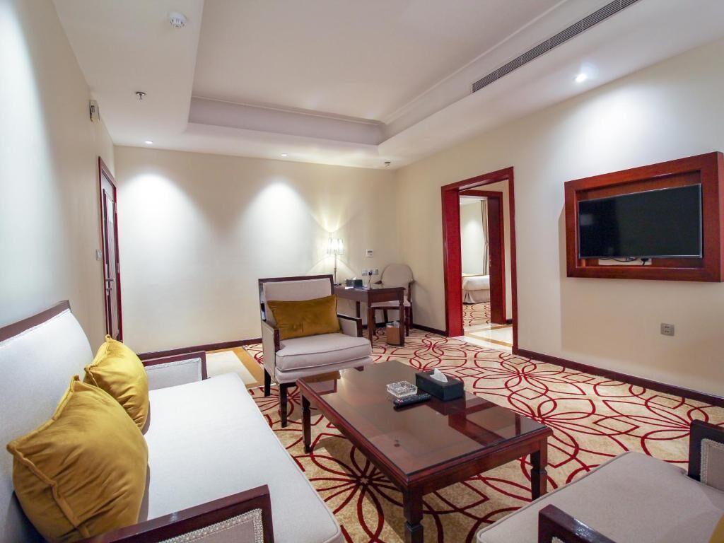 A hotel room with a sofa, a coffee table, a TV, and a patterned carpet.