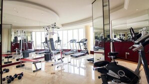 Une salle de sport moderne équipée de machines de cardio, de poids libres et d’un mur avec des miroirs.
