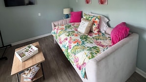 A room with a bed, a TV mounted on the wall, and a wooden coffee table with magazines. - Beach Studio steps to the Beach (Cocoa Beach)