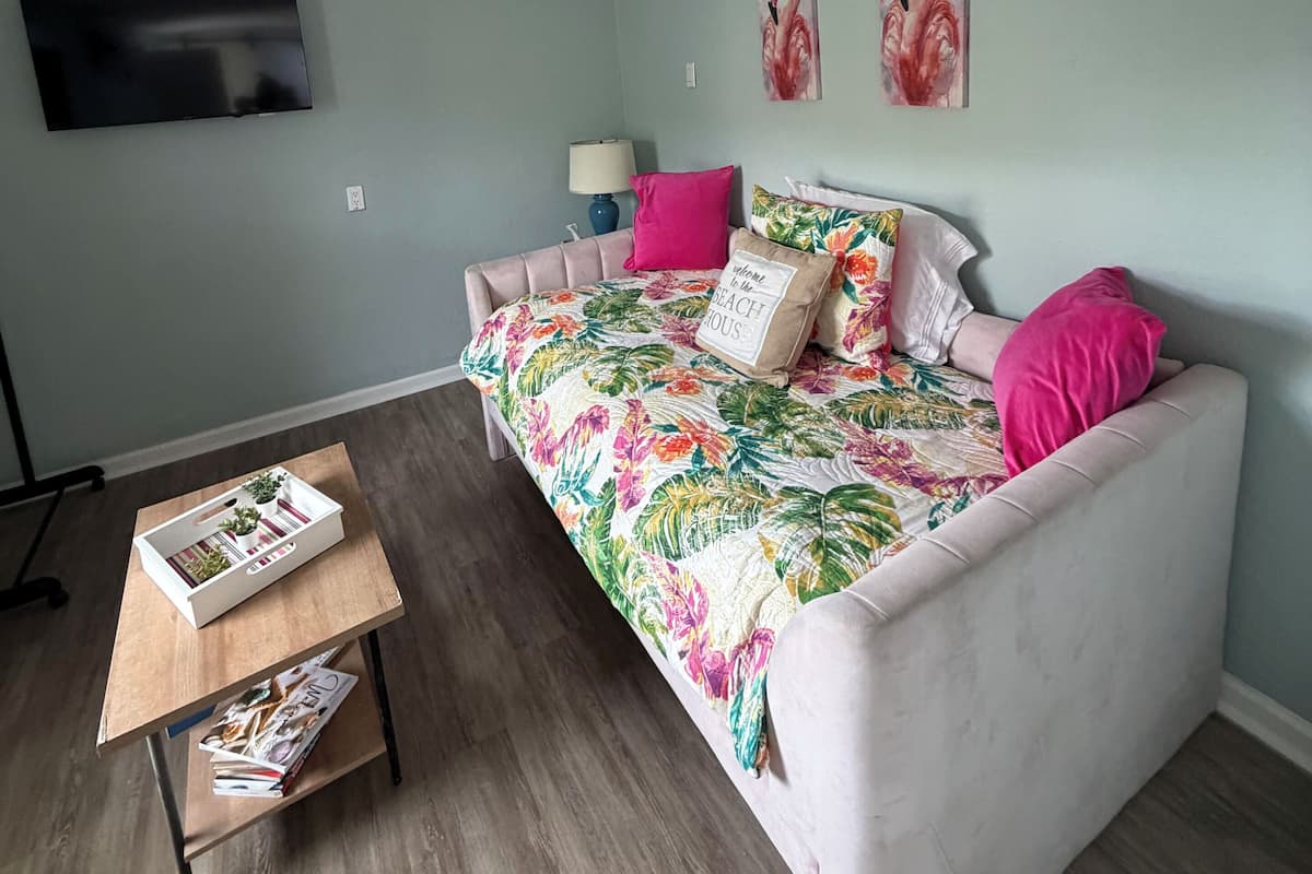 Una habitación con una cama, un televisor montado en la pared y una mesa de centro de madera con revistas.