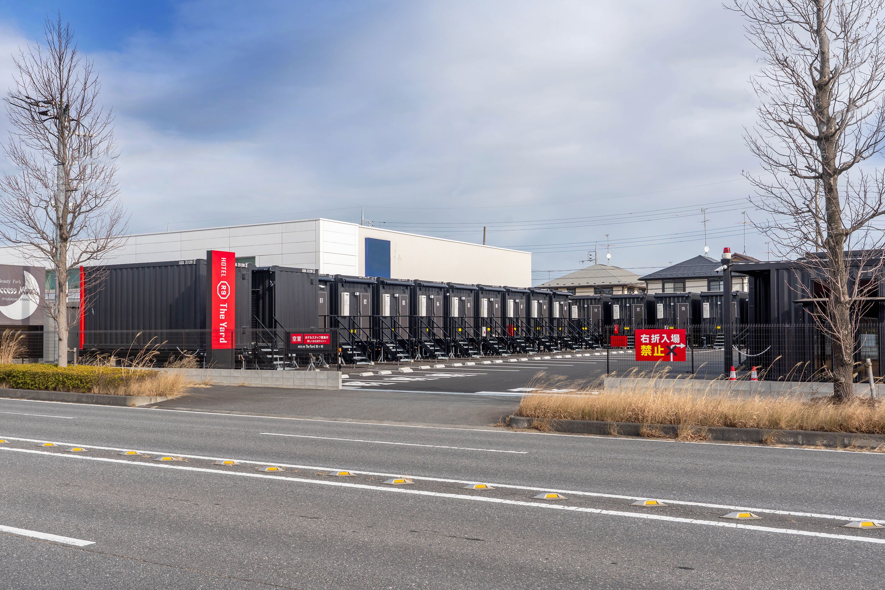 A hotel with a modern design, featuring a prominent red and white sign, a large black building, and a parking area with marked lanes.