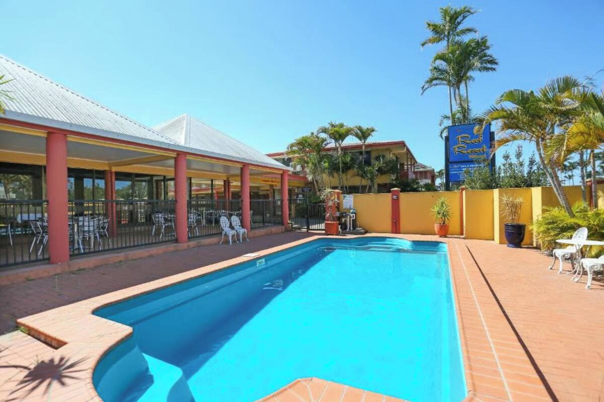 A swimming pool with a covered seating area and palm trees in the background.