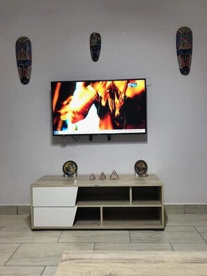 Televisão de tela plana fixada na parede acima de um console de madeira com três objetos decorativos.