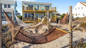 Ein Strandgrundstück mit einem zweistöckigen Haus, einer Hängematte und einer Holzterrasse.