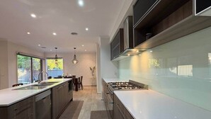 A modern kitchen with a central island, recessed lighting, and a dining area with a view. - Modern Family Haven | Spacious 4BR + Media Room (Tarneit)