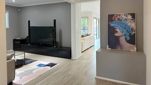 A modern living room with a flat-screen TV, a sofa, and a dining area with a table and chairs. - Modern Family Haven | Spacious 4BR + Media Room (Tarneit)