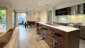 A modern kitchen with a central island, bar stools, and a dining area with chairs. - Modern Family Haven | Spacious 4BR + Media Room (Tarneit)