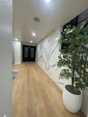 Un pasillo con suelo de madera, una planta en maceta, una pared de mármol y una escalera con barandilla.