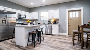 A modern kitchen with white cabinets, stainless steel appliances, and a wooden island with bar stools. - Game Day Getaway • Near Rocky Top Sports World • Sleeps 6 • Quiet Neighborhood (Gatlinburg)