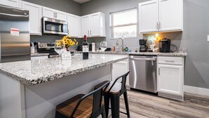 A modern kitchen with white cabinets, a granite countertop, stainless steel appliances, and a bar area with stools. - Game Day Getaway • Near Rocky Top Sports World • Sleeps 6 • Quiet Neighborhood (Gatlinburg)