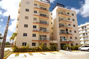 A multi-story hotel with balconies, a parking area, and palm trees. - Punta Cana 3BR Condo - Pool & Jacuzzi - Gated - 15 Min to Bávaro Beach (Punta Cana)