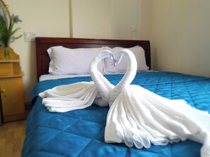 A bed with a blue quilt and white pillows, a wooden headboard, and a decorative towel arrangement in the shape of a swan. - Dong Tay hotel (Quy Nhon)