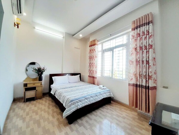 A bedroom with a bed, a bedside table with a mirror, a small cabinet, and a window with curtains.