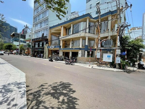 A multi-story hotel with a ground-floor restaurant, outdoor seating, and a parking area with motorcycles.