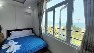 A hotel room with a bed, a view of the sea, and a window with curtains.