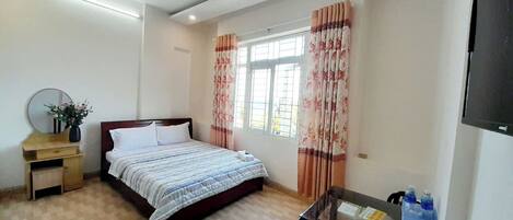 A bedroom with a bed, a nightstand, a desk, a chair, a TV, and a window with curtains.