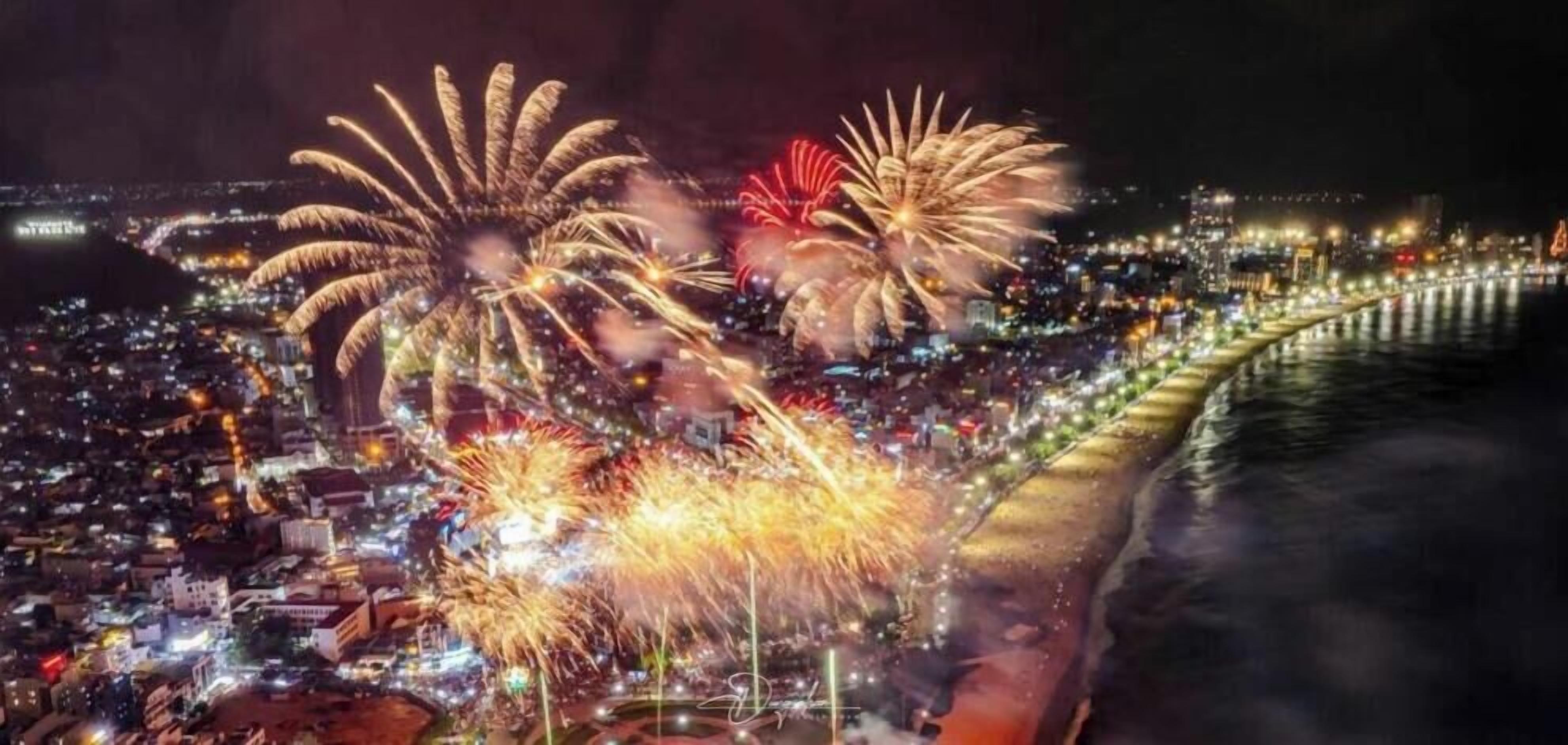 Ein belebtes Stadtbild bei Nacht mit Feuerwerk über einer Uferpromenade.