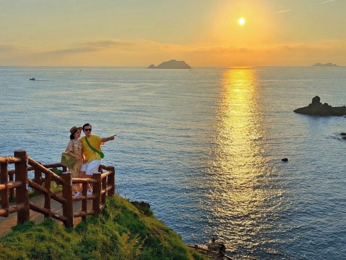 Um deck de madeira com vista para a água, com o pôr do sol ao fundo.
