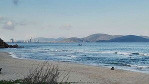 A beach with a clear view of the sea, distant mountains, and a city skyline in the background. - Dong Tay hotel (Quy Nhon)