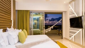 Ein modernes Hotelzimmer mit einem großen Bett, einem Fernseher und einem Balkon mit Blick auf den Abendhimmel.