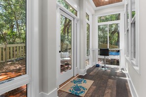 A covered porch with a wooden deck, a chair, and a television. - Enjoy sun-kissed Island days at this recently-built four-bedroom/ 3.5-bath (Bald Head Island)