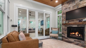 A living room with a fireplace, a sofa, a chair, and a TV mounted on the wall. - Enjoy sun-kissed Island days at this recently-built four-bedroom/ 3.5-bath (Bald Head Island)