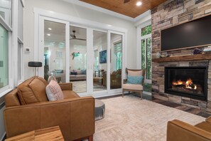 A living room with a fireplace, a sofa, a chair, and a TV mounted on the wall. - Enjoy sun-kissed Island days at this recently-built four-bedroom/ 3.5-bath (Bald Head Island)
