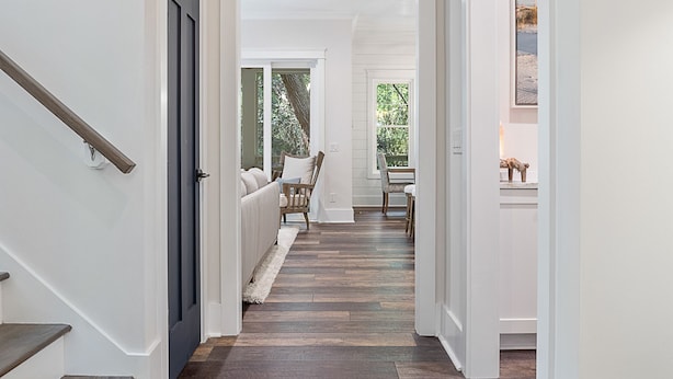 A hallway with a wooden staircase, a cushioned bench, and a view of an outdoor area with greenery. - Enjoy sun-kissed Island days at this recently-built four-bedroom/ 3.5-bath (Bald Head Island)