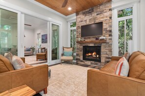 A living room with a stone fireplace, leather sofas, and a large TV. - Enjoy sun-kissed Island days at this recently-built four-bedroom/ 3.5-bath (Bald Head Island)