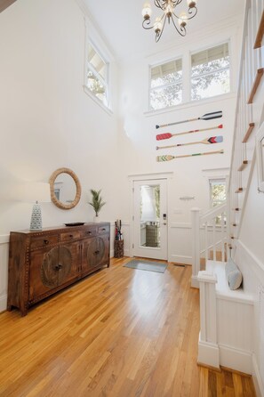 A spacious room with wooden flooring, a white staircase, and a collection of paddles on the wall. - Nestled amongst the oaks and palms of the maritime forest, this charming four-bedroom (Bald Head Island)