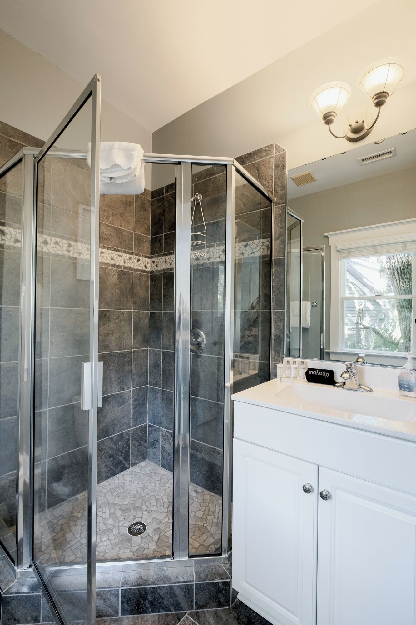 A modern bathroom with a glass-enclosed shower, a white vanity with a mirror, and a chandelier.