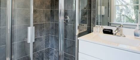 A modern bathroom with a glass-enclosed shower, a white vanity with a mirror, and a chandelier.